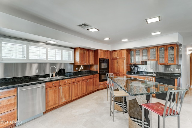 kitchen with stainless steel dishwasher, double oven, dark stone countertops, and sink