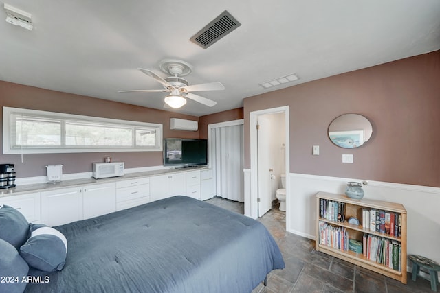 bedroom with a wall mounted air conditioner, ceiling fan, and ensuite bath