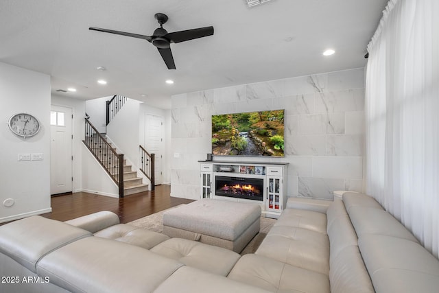 living area with a warm lit fireplace, ceiling fan, wood finished floors, stairs, and recessed lighting