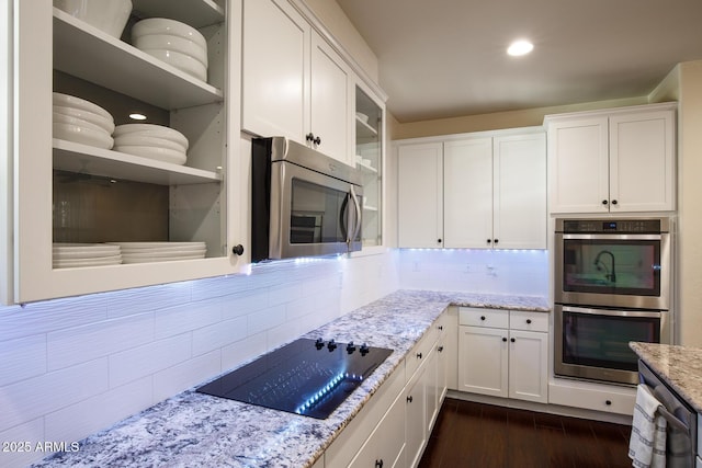 kitchen with light stone countertops, stainless steel appliances, dark wood-type flooring, white cabinetry, and decorative backsplash