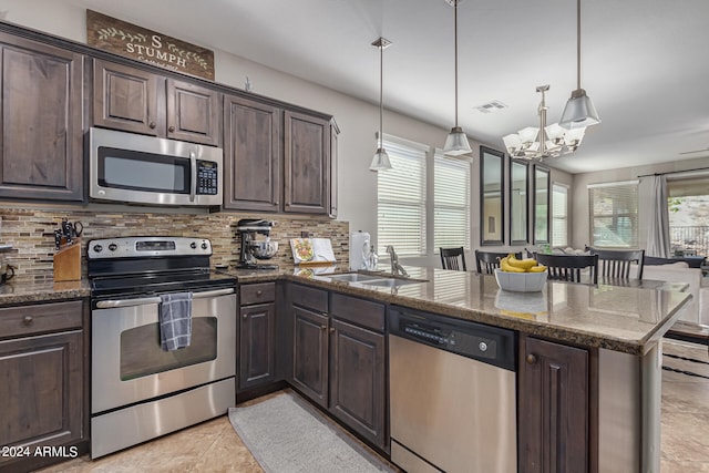 kitchen with dark stone countertops, stainless steel appliances, decorative light fixtures, and kitchen peninsula