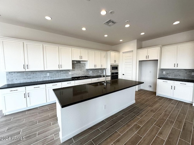 kitchen with sink, white cabinets, decorative backsplash, a kitchen island with sink, and stainless steel appliances