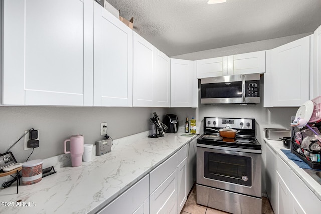 3646 N 67th Ave Unit 29, Phoenix, AZ 85033 - kitchen with stainless steel appliances, white cabinetry, light stone countertops, a textured ceiling, and light tile patterned floors
