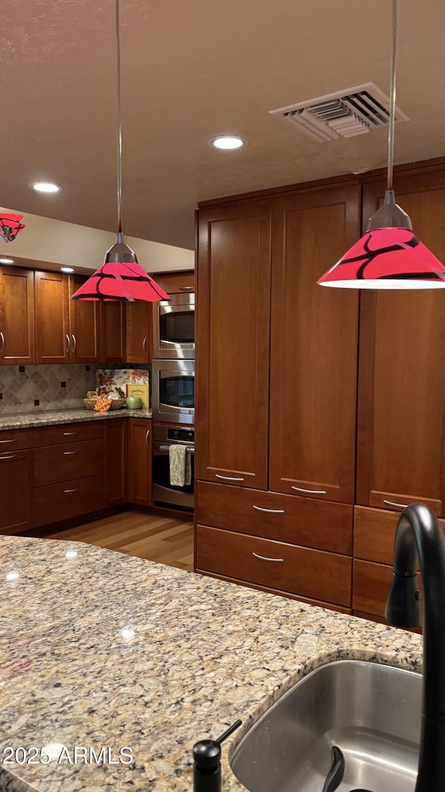 8426 N 15th Dr, Phoenix, AZ 85021 - kitchen featuring stainless steel appliances, visible vents, decorative backsplash, pendant lighting, and brown cabinetry