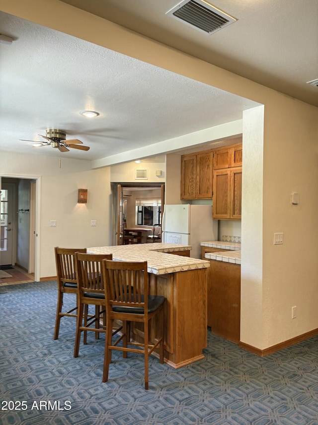 8426 N 15th Dr, Phoenix, AZ 85021 - kitchen with a kitchen breakfast bar, brown cabinetry, dark colored carpet, visible vents, and freestanding refrigerator