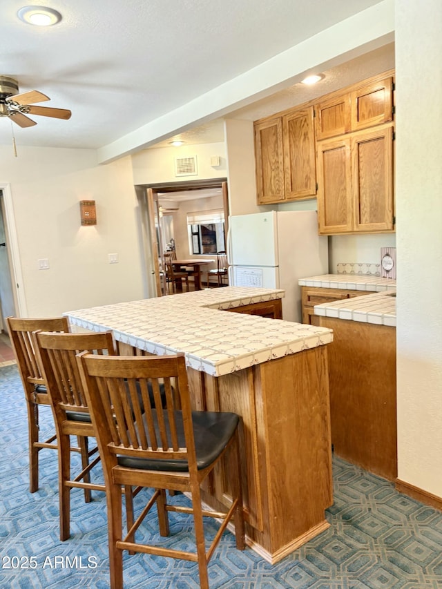 8426 N 15th Dr, Phoenix, AZ 85021 - kitchen featuring a center island, freestanding refrigerator, ceiling fan, tile counters, and a breakfast bar area