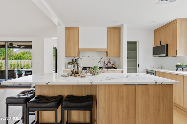 kitchen featuring light stone countertops, light brown cabinetry, a breakfast bar, ceiling fan, and a kitchen island