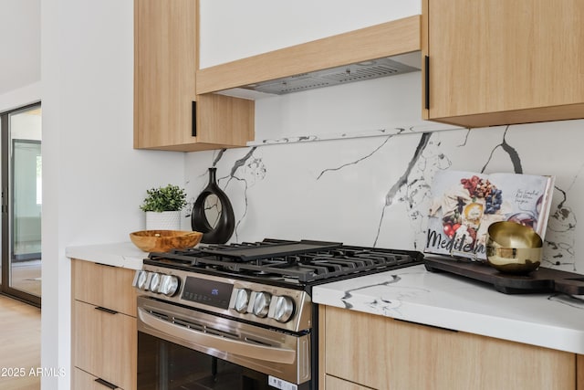 kitchen with light stone counters, light brown cabinets, exhaust hood, and stainless steel range with gas stovetop