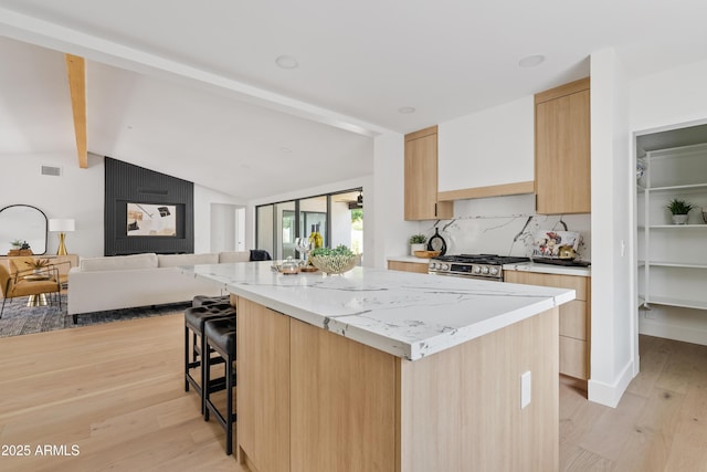 kitchen with backsplash, stainless steel range with gas cooktop, light hardwood / wood-style flooring, light brown cabinetry, and a breakfast bar area