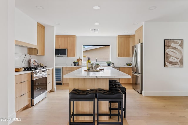 kitchen with light wood-type flooring, appliances with stainless steel finishes, a kitchen island, a breakfast bar area, and beverage cooler