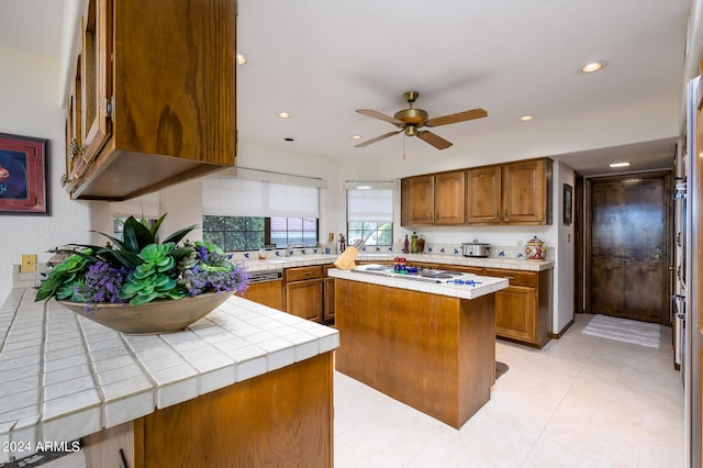 kitchen featuring a kitchen island, ceiling fan, tile countertops, white gas cooktop, and light tile floors