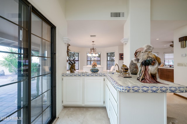 kitchen with white cabinets, sink, ceiling fan with notable chandelier, decorative light fixtures, and kitchen peninsula