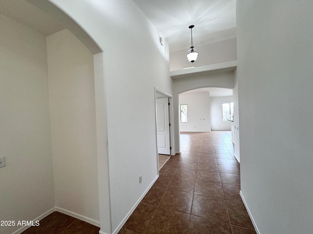 hall featuring arched walkways, dark tile patterned floors, and baseboards