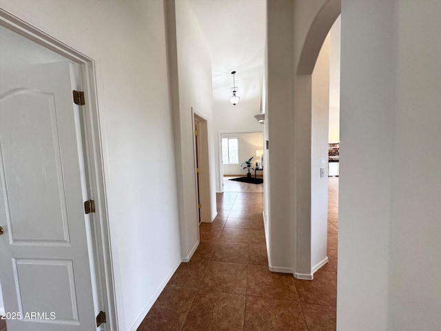 hallway with dark tile patterned floors, arched walkways, and baseboards