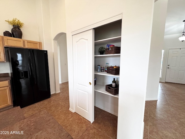 interior space featuring arched walkways, a high ceiling, black fridge with ice dispenser, baseboards, and dark countertops