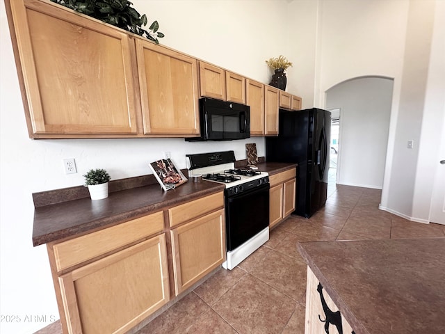 kitchen featuring arched walkways, light tile patterned floors, a high ceiling, black appliances, and dark countertops