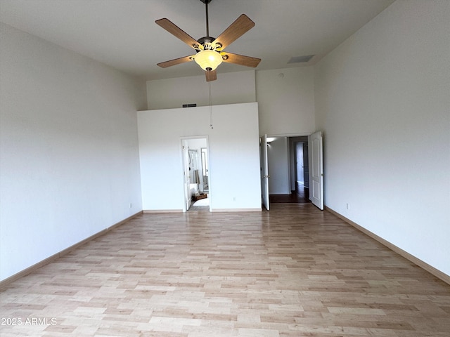 empty room featuring ceiling fan, a towering ceiling, visible vents, baseboards, and light wood finished floors