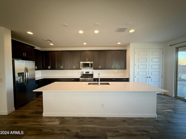 kitchen featuring a center island with sink, sink, decorative backsplash, appliances with stainless steel finishes, and dark hardwood / wood-style flooring