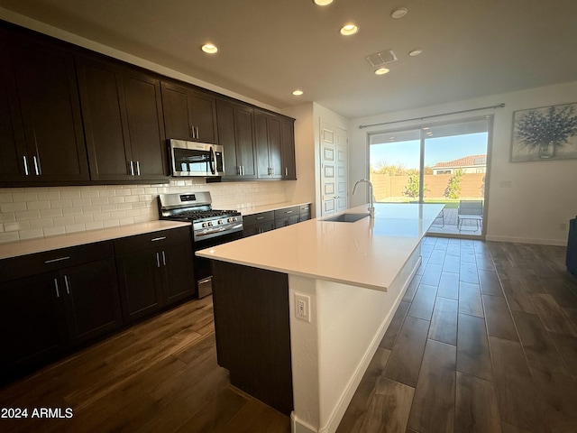 kitchen with dark hardwood / wood-style flooring, backsplash, stainless steel appliances, sink, and a center island with sink