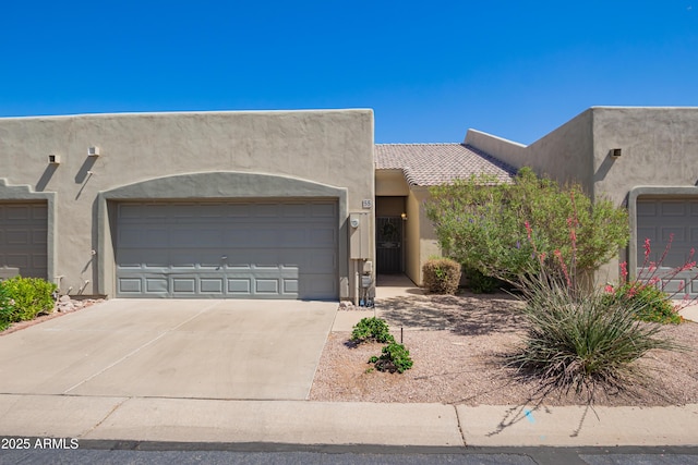 pueblo revival-style home with stucco siding, driveway, and a garage