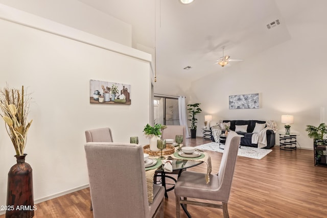 dining area featuring wood finished floors, a ceiling fan, baseboards, and vaulted ceiling
