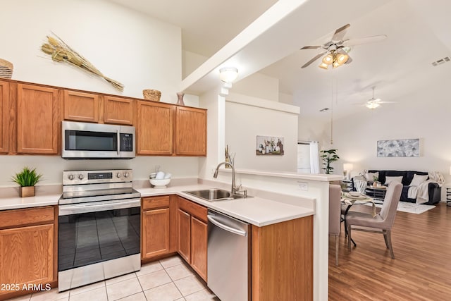 kitchen with stainless steel appliances, a sink, a peninsula, open floor plan, and a ceiling fan