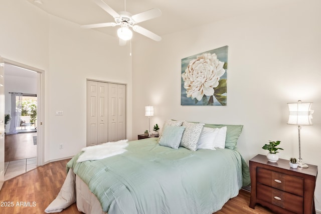 bedroom featuring wood finished floors, a closet, ceiling fan, and a high ceiling