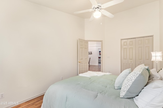 bedroom with light wood finished floors, a towering ceiling, a closet, baseboards, and ceiling fan
