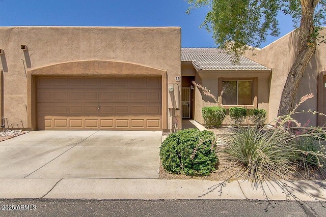 pueblo-style home featuring stucco siding, concrete driveway, a garage, and a tile roof