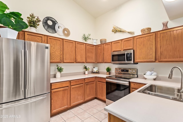 kitchen featuring appliances with stainless steel finishes, a sink, vaulted ceiling, brown cabinets, and light countertops