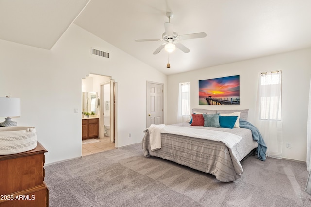 bedroom featuring light carpet, vaulted ceiling, ensuite bathroom, and a ceiling fan