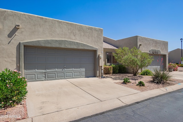 pueblo-style house featuring driveway, stucco siding, and an attached garage