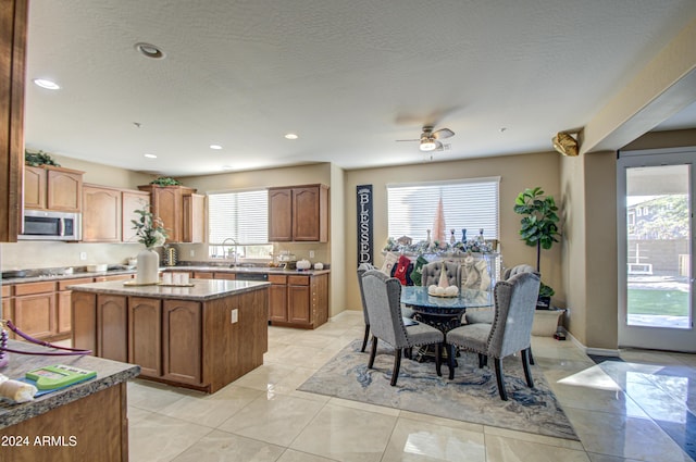 kitchen featuring a textured ceiling, a kitchen island, ceiling fan, and light stone counters