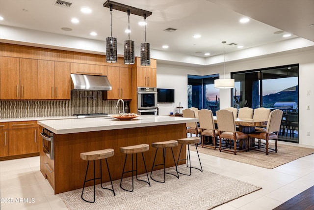 9894 E Miramonte Dr, Scottsdale, AZ 85262 - kitchen featuring ventilation hood, brown cabinets, light countertops, and a kitchen island with sink