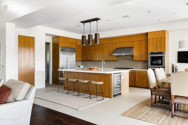 9894 E Miramonte Dr, Scottsdale, AZ 85262 - kitchen featuring stainless steel appliances, wine cooler, under cabinet range hood, light countertops, and brown cabinetry