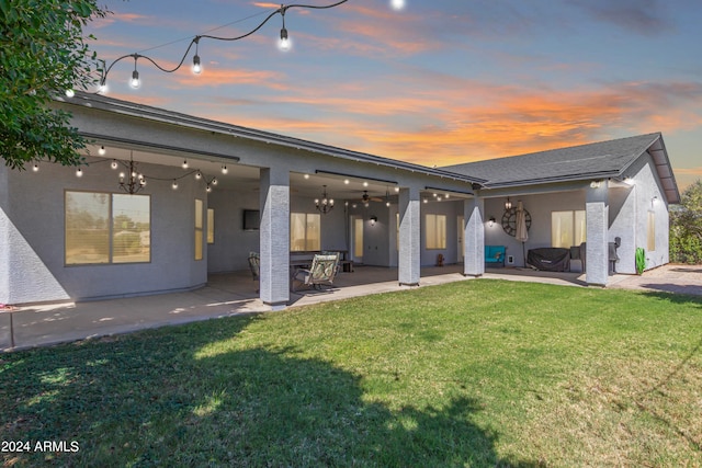 back house at dusk featuring a patio and a lawn