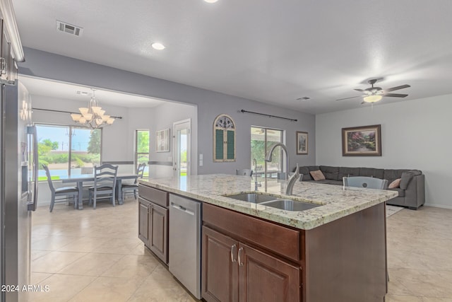 kitchen featuring sink, light stone counters, an island with sink, ceiling fan with notable chandelier, and appliances with stainless steel finishes