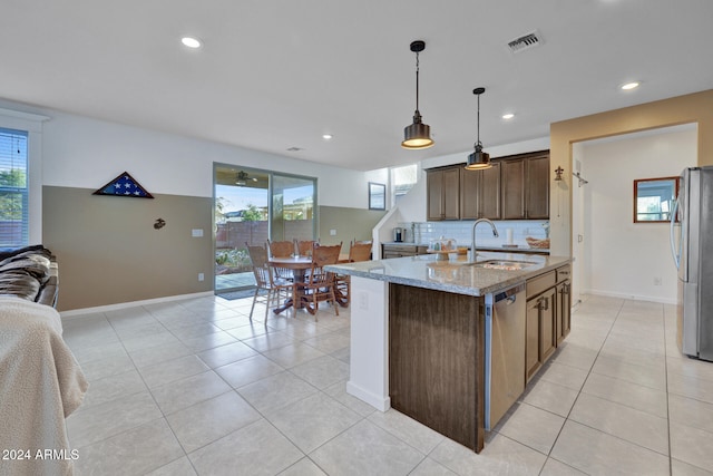 kitchen with appliances with stainless steel finishes, light stone countertops, decorative light fixtures, a kitchen island with sink, and sink