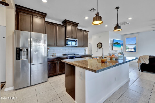 kitchen featuring dark stone counters, dark brown cabinets, sink, an island with sink, and stainless steel appliances