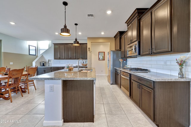 kitchen with light stone countertops, pendant lighting, stainless steel appliances, dark brown cabinets, and sink