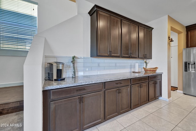 kitchen with dark brown cabinetry, light tile patterned floors, light stone countertops, and stainless steel fridge with ice dispenser