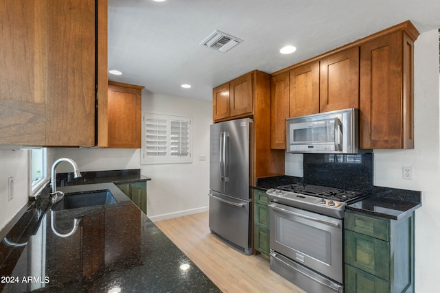 kitchen with backsplash, stainless steel appliances, light hardwood / wood-style flooring, dark stone counters, and sink