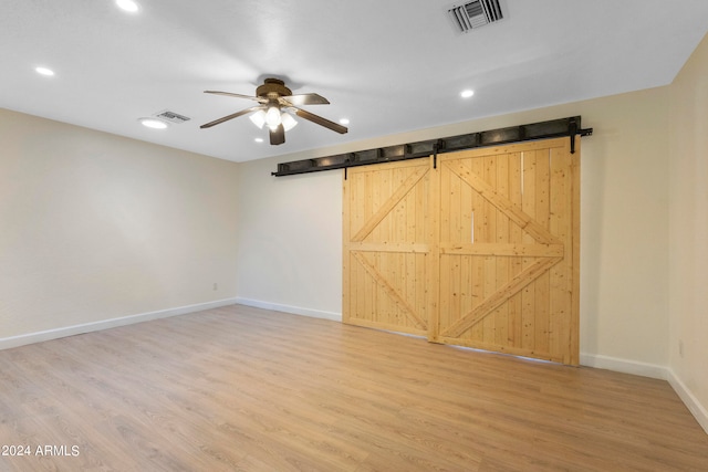 unfurnished room featuring ceiling fan, a barn door, and wood-type flooring