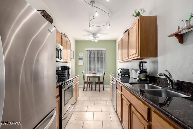 kitchen with light tile patterned floors, ceiling fan, stainless steel appliances, dark stone countertops, and sink