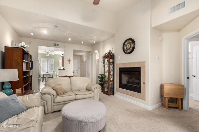 living room with ceiling fan, light colored carpet, and a tiled fireplace