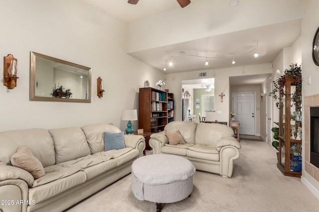 living room with ceiling fan, light colored carpet, and a tiled fireplace