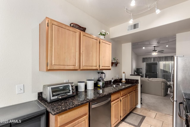 kitchen featuring stainless steel fridge, ceiling fan, dishwashing machine, dark stone counters, and sink