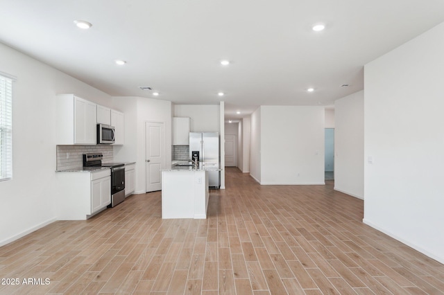 17806 W Vogel Ave, Waddell, AZ 85355 - kitchen featuring appliances with stainless steel finishes, open floor plan, backsplash, a kitchen island with sink, and white cabinets