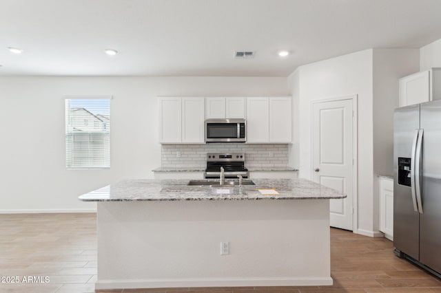 17806 W Vogel Ave, Waddell, AZ 85355 - kitchen with appliances with stainless steel finishes, light wood-style flooring, decorative backsplash, light stone counters, and an island with sink