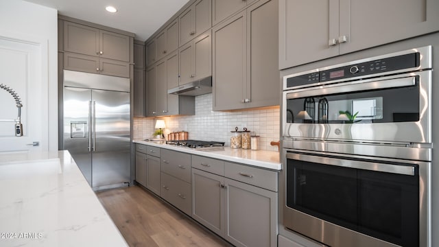 kitchen featuring light wood-type flooring, stainless steel appliances, light stone counters, and gray cabinets